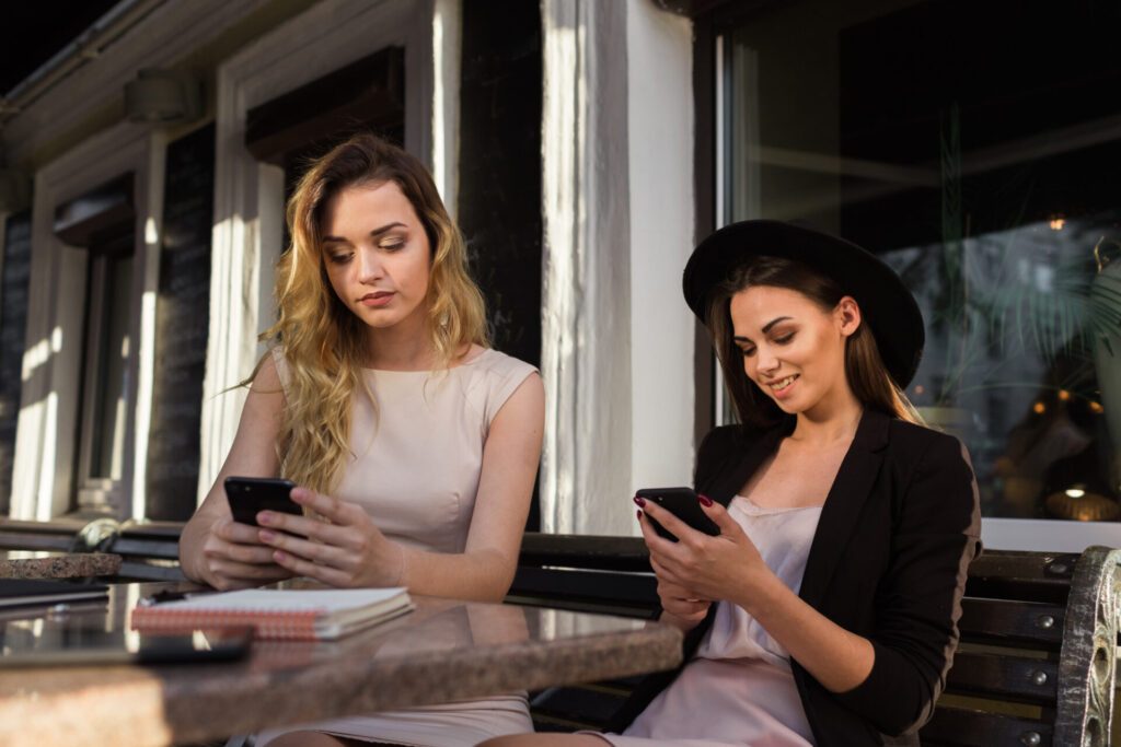 two women sitting at a table looking at their phones. immersion techniques for quick learning