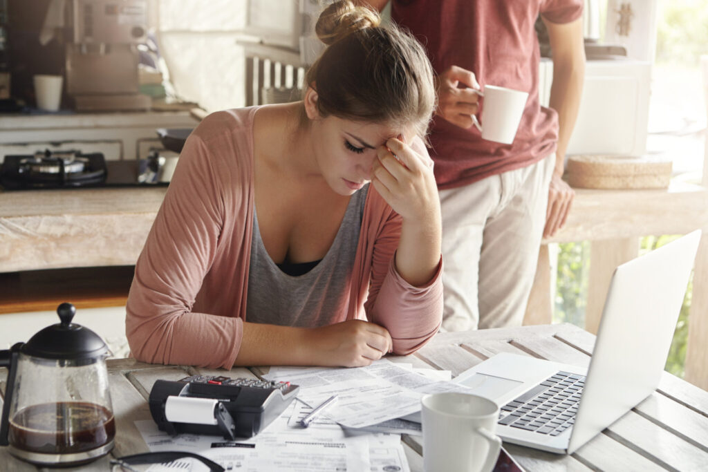 a woman sitting at a table with a laptop and papers - stop overspending now