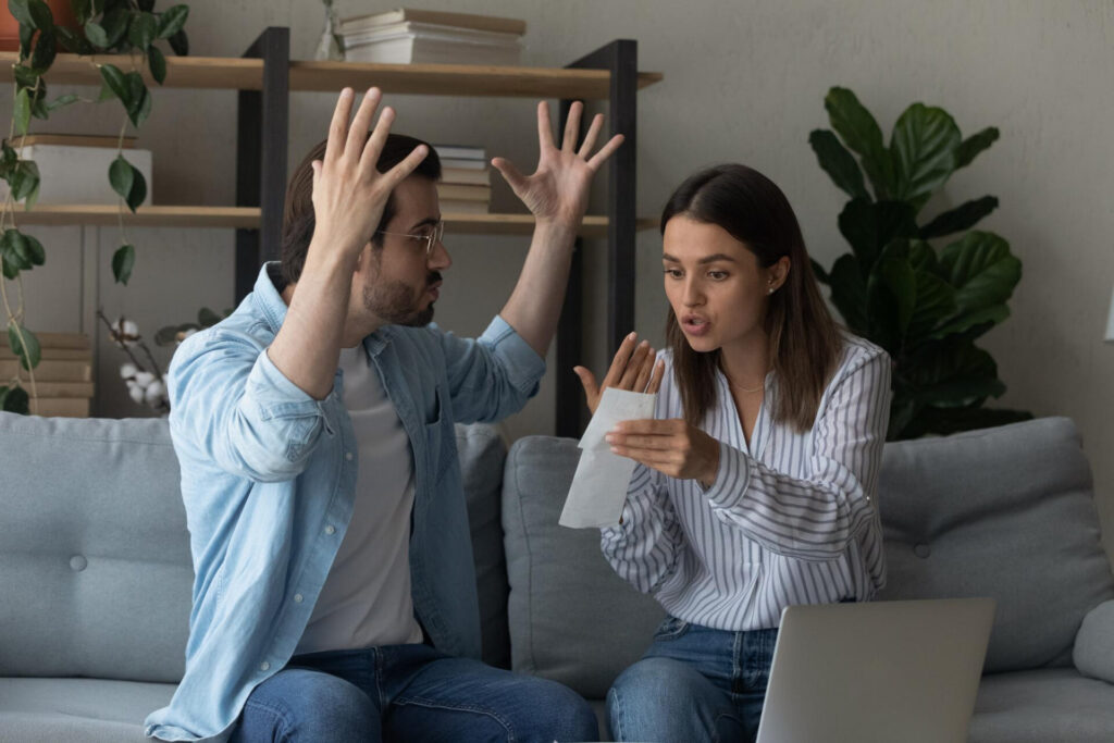 how to resolve relationship conflict: a man and woman sitting on a couch with hands up