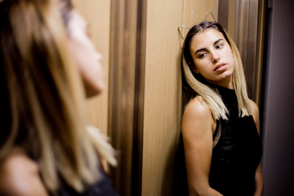 a woman leaning on a wall looking at herself - stop self-sabotaging your success