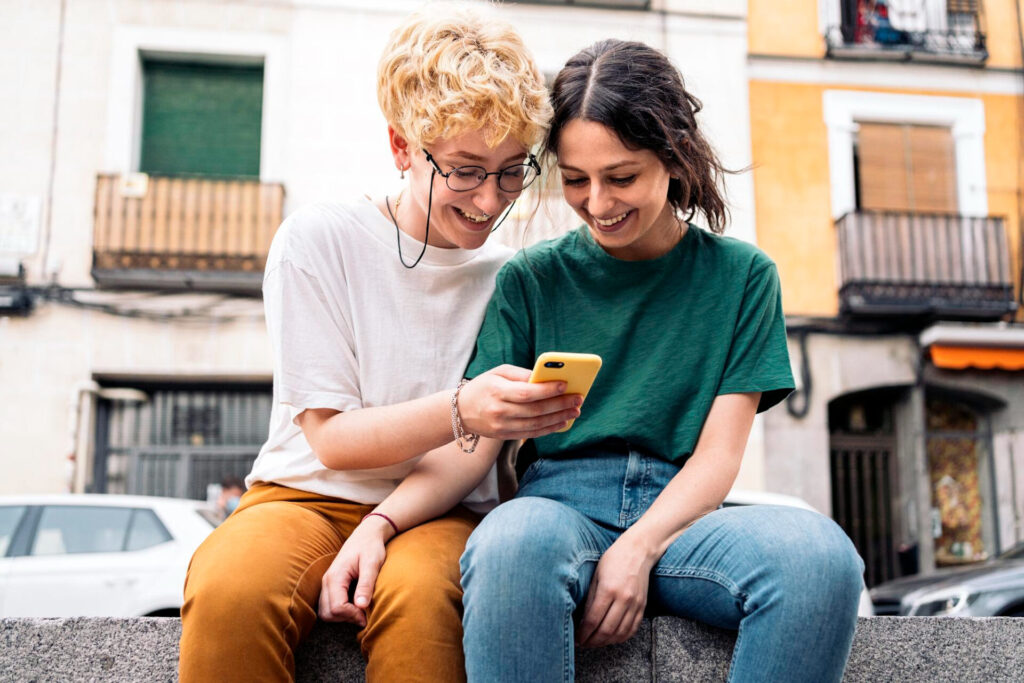 understanding language barriers. two women sitting on a ledge looking at a phone