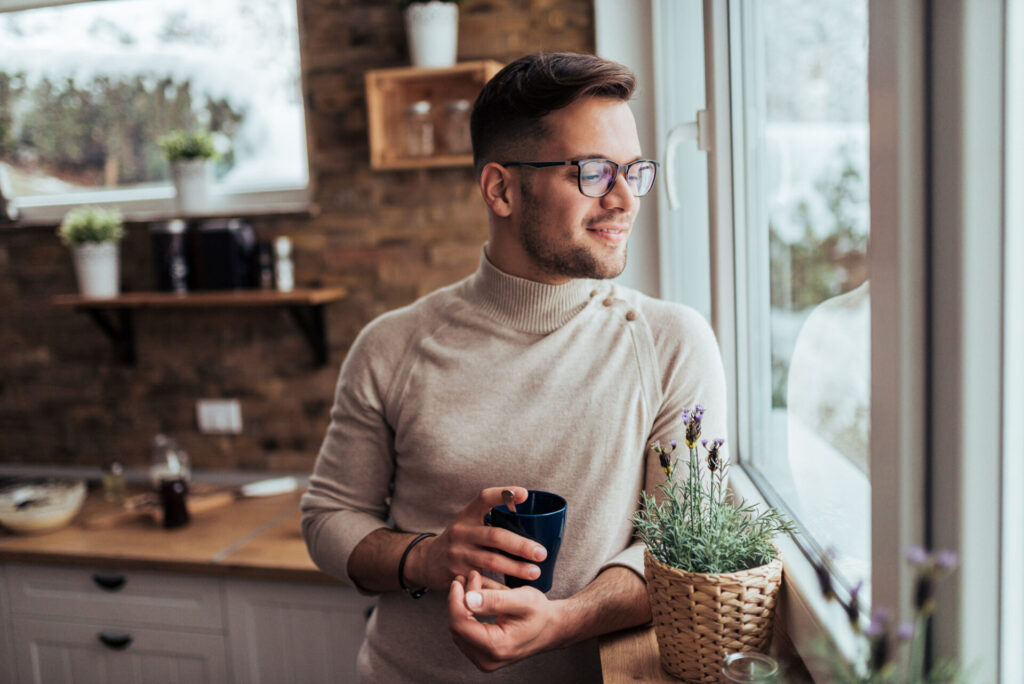 a man holding a cup looking out a window