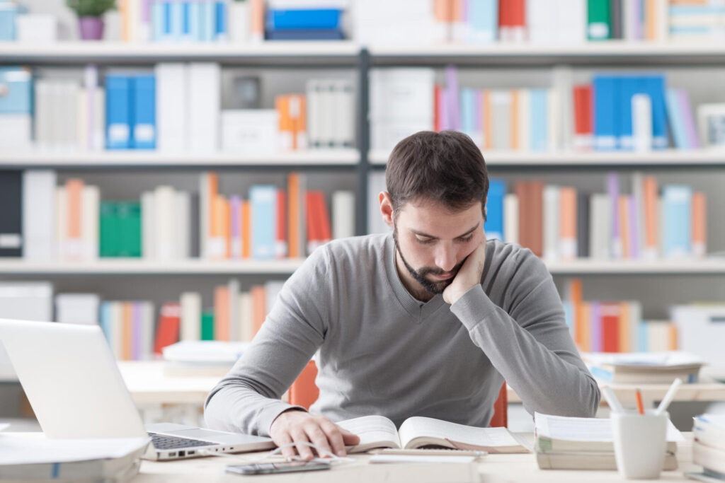 a young man in a library reading a book - best way to learn new skills independently