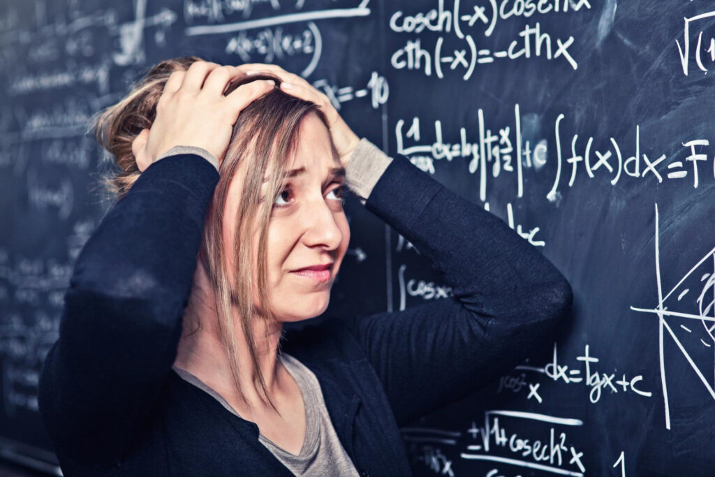 a woman holding her head in front of a chalkboard - how to overcome math anxiety permanently