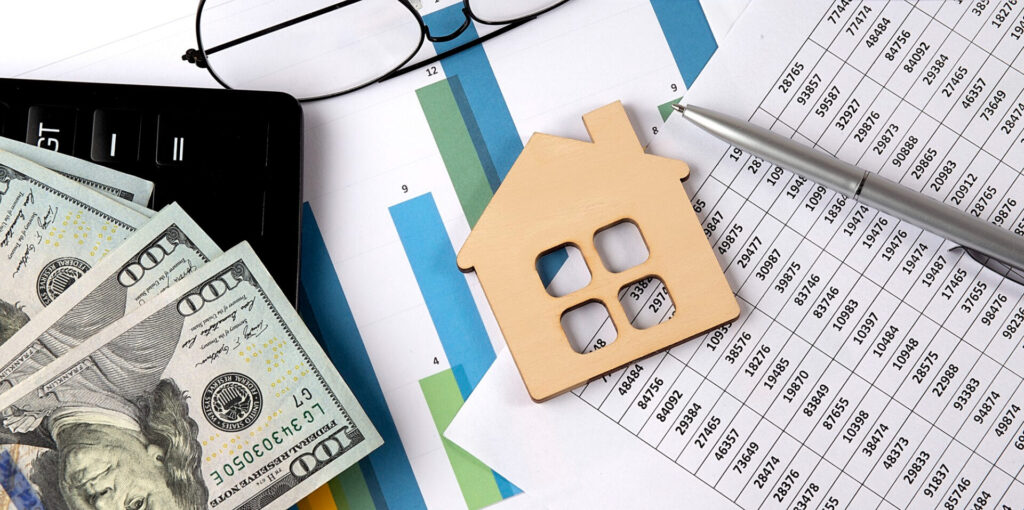 Finance - a wooden house on a paper with a pen and glasses