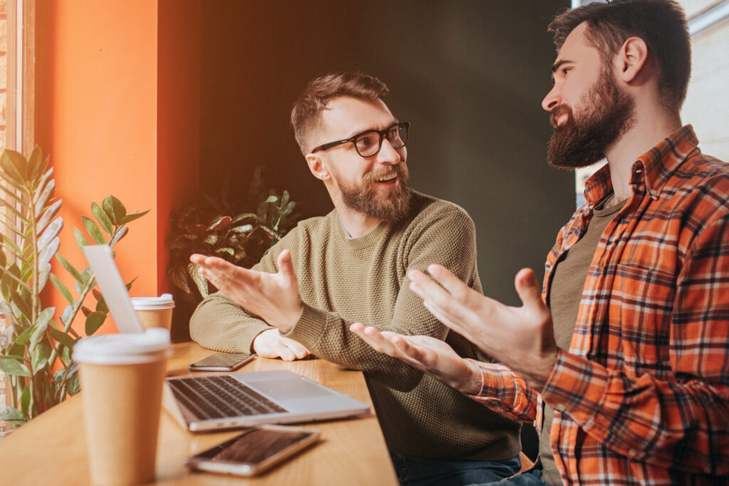 two men sitting at a table with a laptop