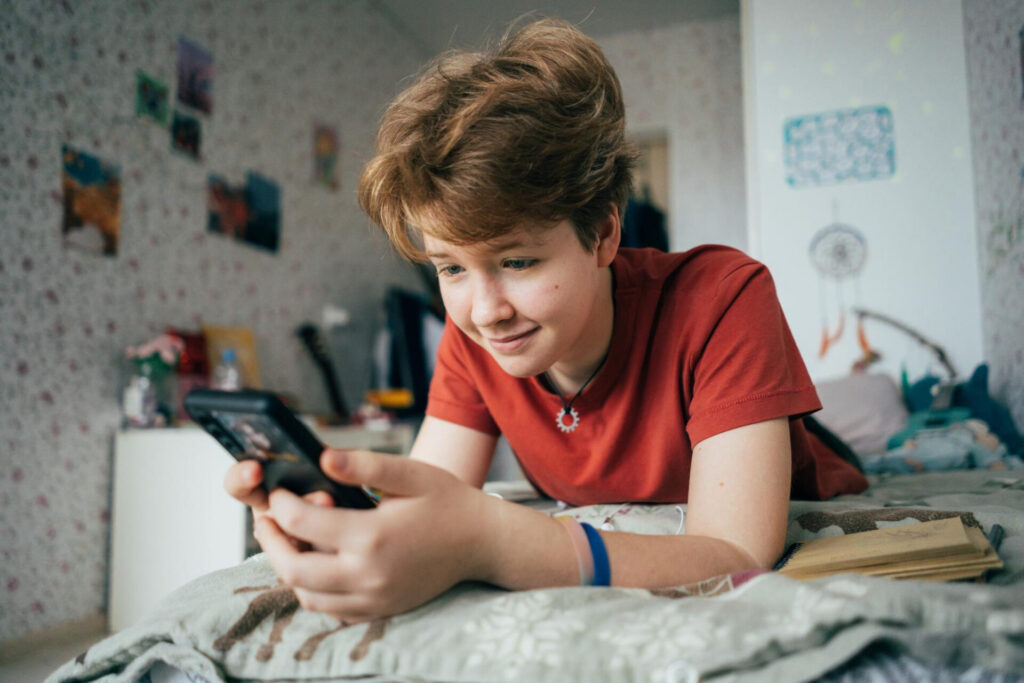 a boy lying on a bed looking at a phone