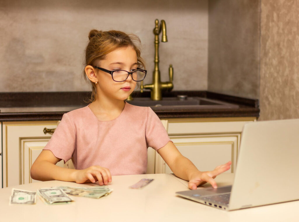 a girl sitting at a table with a laptop and money