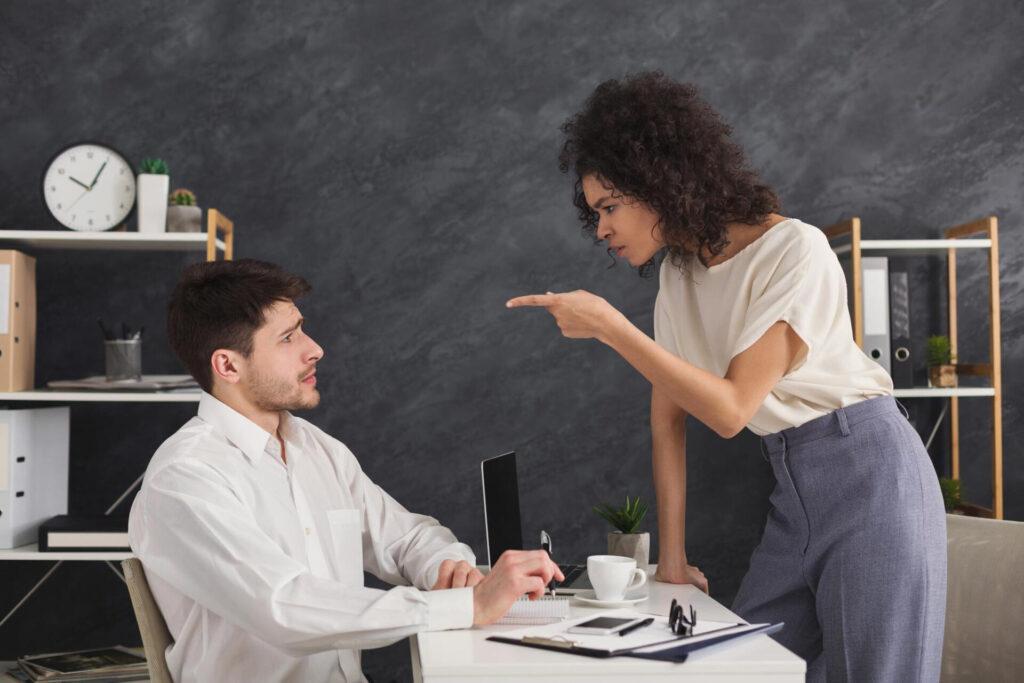 how to be assertive without being aggressive: a woman pointing at a man at a desk